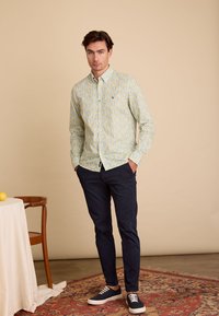 Lichtblauw en gele gestreepte button-up shirt, donkerblauwe broek en donkerblauwe sneakers. Kenmerkt zich door een klein logo en een ontspannen fit.