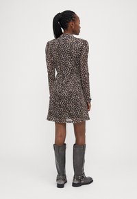 Robe à imprimé léopard avec des manches longues, taille cintrée et ourlet fluide ; associée à des bottes grises jusqu'aux genoux avec des boucles et un talon épais.