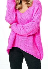 Svetle růžový pletený svetr s výstřihem do V a oversized střihem. Obsahuje volné rukávy a asymetrický spodní lem, kombinovaný s černými džíny.
