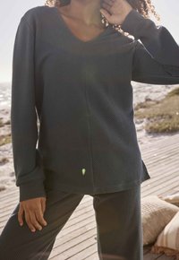 Maglia a maniche lunghe di un verde scuro, a coste, con scollatura a V, caratterizzata da una cucitura diagonale e un fit rilassato. Abbinata a pantaloni coordinati a coste.