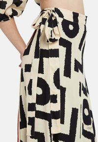 Falda maxi en una tela crema con un audaz patrón abstracto negro, que presenta un lazo en la cintura y detalles plisados para añadir textura.