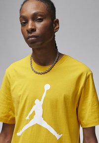 T-shirt di cotone gialla con un grande logo Jumpman bianco stampato sul davanti. Presenta un colletto tondo e maniche corte. Tessuto testurizzato.