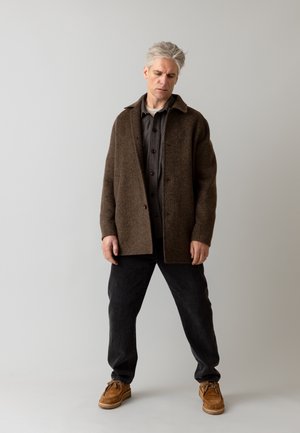 Smeđi vuneni kaput s ovratnikom, sivi košulja s dugim rukavima, crne hlače i smeđe cipele. Jednostavan kroj, bez vidljivih uzoraka, teksturirana tkanina.