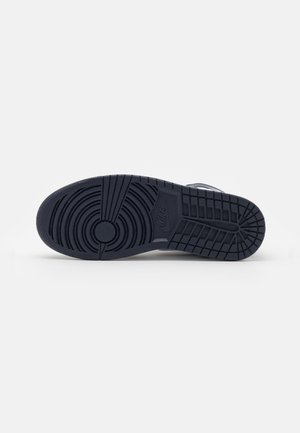 Semelle d'une basket Nike de couleur sombre avec des motifs de bande de roulement circulaires et en grille sur un fond clair uni.