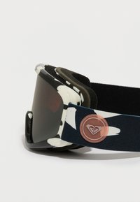 Óculos de esqui com um padrão a preto e branco, lentes escuras tintadas, almofadado macio em espuma e uma correia azul ajustável com detalhe de logótipo.