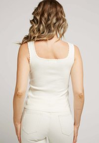 Débardeur ajusté blanc avec un décolleté carré et un ourlet festonné, fabriqué dans un tissu ribbed léger. Porté avec un pantalon de couleur claire.