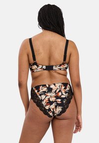 Set bikini a fantasia floreale in nero e beige, con pizzo sui pantaloni e spalline regolabili sulla parte superiore. Visuale da dietro mostrata.