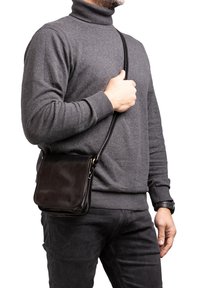 Borsa a tracolla in pelle marrone con finitura liscia, forma rettangolare, tracolla staccabile e design minimalista, indossata su un maglione grigio.