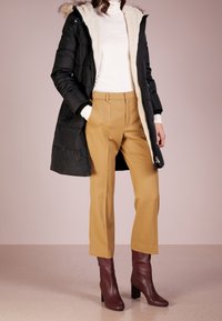 Svart puffjacka med fuskpälsfoder, vit polotröja, senapsgula byxor och burgunderfärgade klackstövlar. Slät textur och åtsittande design.