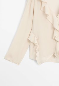 Blusa beige chiaro con maniche lunghe, dotata di un collo arricciato e una patta frontale. Realizzata in un tessuto liscio e leggero.