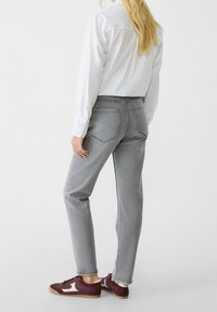 Jeans grises de corte recto con costuras visibles, combinados con una camisa blanca de botones y unas zapatillas burdeos, que muestran un look casual.