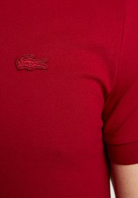 Röd polo tröja med strukturerad tyg. Broderad logotyp i matchande röd på vänster sida av bröstet. Korta ärmar, klassisk krage.