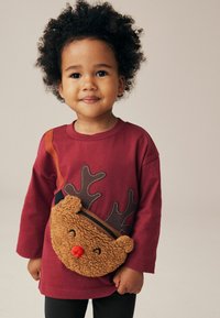 Chemise à manches longues bordeaux avec un design d'anticorne, associée à un sac en peluche marron en forme de renne avec un nez rouge et une sangle noire.
