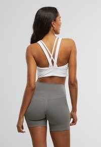 Hvit sports-bh med kryssede stropper, parret med høytlivede grå shorts, glatt tekstur, tettsittende design, minimalistisk stil.