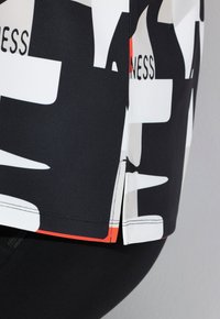 Maglietta sportiva multicolore con base nera e pattern astratti bianchi e arancioni, realizzata in un tessuto elastico e liscio con aperture laterali.