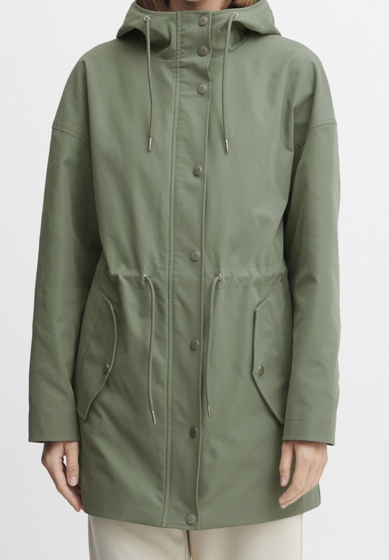 Giacca parka verde realizzata in un morbido tessuto testurizzato. Presenta un cappuccio con cordino, bottoni a pressione e due tasche frontali con toppe.