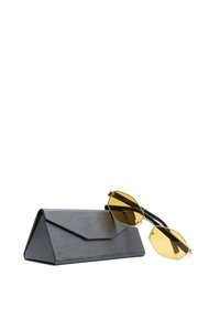 Custodia per occhiali nera con texture triangolare, con occhiali da sole pieghevoli con lenti giallo-tingente appoggiati sopra, su sfondo bianco.