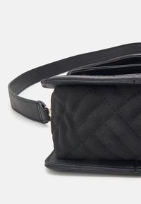 Svart quiltad handväska med slät läderdetalj. Har en platt design och ett avtagbart band för crossbody- eller axelbärare.