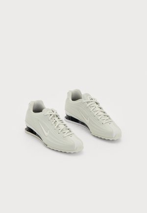 White Nike sneakers with a textured upper, featuring a smooth toe cap and black cushioning accents. Lace-up style with a reinforced heel.
