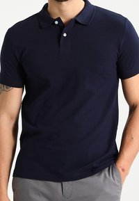 Polo bleu marine en coton, à manches courtes, avec un col, deux boutons et un logo discret sur la poitrine. Texture lisse.