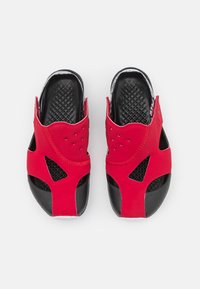 Röda gummisandaler med svarta texturerade sulor och urklippta mönster. Har perforeringar för ventilation och böjda kanter.