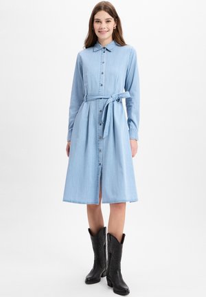 Helles denimhemdkleid mit langen Ärmeln, Knopfverschluss vorne und einem gebundenen Taillengürtel. Verfügt über einen Kragen und einen ausgestellten Rock. Kombiniert mit schwarzen Cowgirl-Stiefeln.