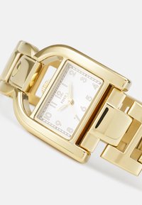 Goldfarbene Metalluhr mit rechteckigem Ziffernblatt, weißem Ziffernblatt und arabischen Ziffern. Massives Gliederarmband im polierten Finish.
