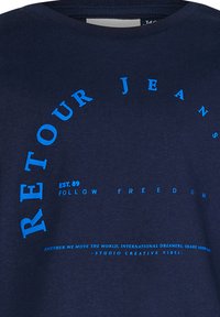 Marineblaue Baumwoll-T-Shirt mit blauem, kreisförmigem Textdesign, das "RETOUR JEANS", "EST.89" und "FOLLOW FREEDOM" deutlich bedruckt hat.
