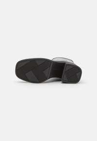Sole nera piatta in gomma testurizzata, con un motivo geometrico. Linee pulite e bordi arrotondati definiscono il suo design minimalista.
