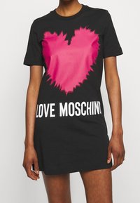 Czarna bawełniana sukienka t-shirtowa z różowym graficznym sercem o poszarpanej krawędzi i białym napisem "LOVE MOSCHINO" na dole. Krótkie rękawy.