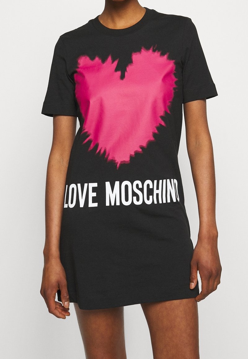 Czarna bawełniana sukienka t-shirtowa z różowym graficznym sercem o poszarpanej krawędzi i białym napisem "LOVE MOSCHINO" na dole. Krótkie rękawy.