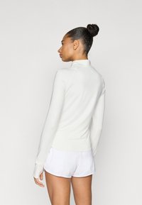 Μπλουζάκι με μακριά μανίκια και ψηλό λαιμό, από απαλό λευκό ύφασμα. Διαθέτει εφαρμοστή γραμμή, λεία υφή και επίπεδα ραφές, σε συνδυασμό με λευκό σορτς.