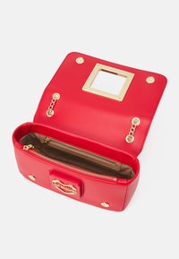 Borsa a mano in pelle sintetica rossa con dettagli in metallo dorato, tasca con zip e interno aperto. Presenta un ritaglio quadrato sul cappuccio.