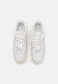 Un par de zapatillas Nike Air Force 1 blancas con cordones, vistas desde arriba, sobre un fondo blanco liso.