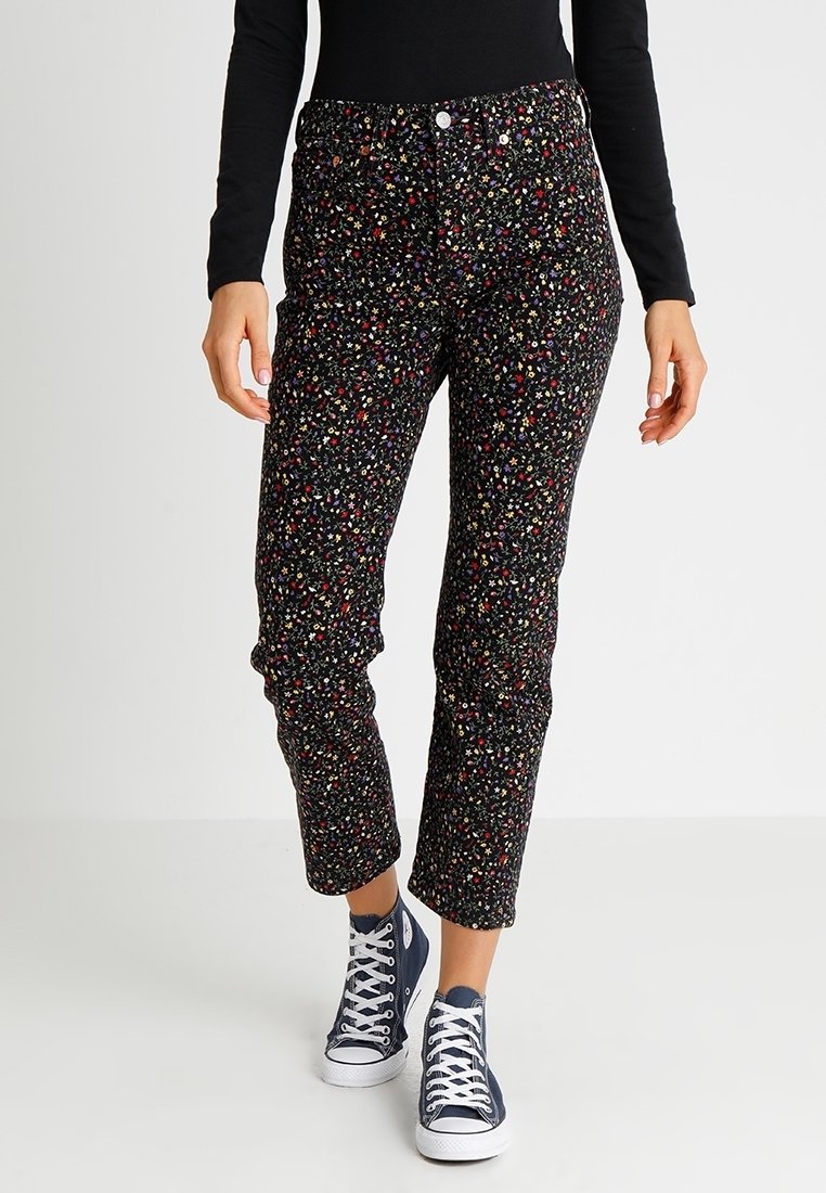 Pantalones negros con un patrón floral en múltiples colores, que cuentan con un corte ajustado y longitud recortada, combinados con zapatillas de alta corte en color navy.