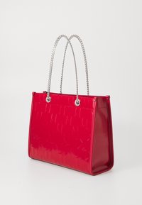 Sac cabas rouge avec un extérieur lisse et brillant, motif géométrique en relief, doubles poignées en chaîne argentée, et une forme structurée.