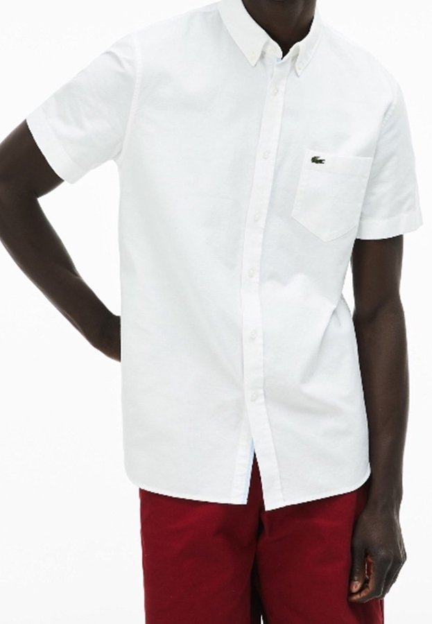 Biała koszula na krótki rękaw z guzikiem, wykonana z bawełny, z kieszonką na piersi i małym zielonym logo. Połączona z czerwonymi spodniami.