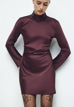 Vestido largo de satén burdeos con mangas largas, cuello alto y silueta ajustada. Presenta una textura suave y una longitud corta, combinado con medias estampadas.