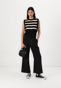 Sort og creme striped ærmeløs striktop parret med brede sorte bukser og sorte Converse sneakers, mens der holdes en lille struktureret sort taske.