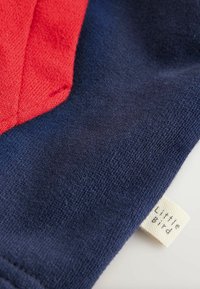 Dzianina w kolorach czerwonym i granatowym o fakturowanym wyglądzie. Zawiera małą, kremową metkę z napisem "Little Bird".