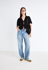 Černý top s krátkými rukávy a krajkovými detaily, světle modré volné džíny a zelenobílé tenisky. Černá kabelka a velké brýle.