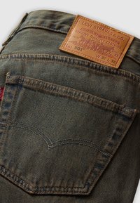 Levi's 501 jeans hebben een klassieke blauwe denim stof, leren patch, oranje stiksels en een onderscheidend ontwerp van de achterzak met een gebogen naad.