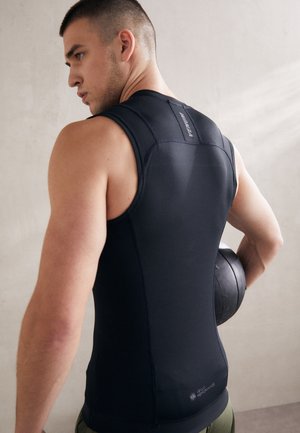 Débardeur de sport sans manches noir, au design ajusté, en matériau lisse. Présente un logo sur l'épaule et un col haut, associé à un ballon de médecine sombre.