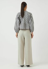 Blusa a maniche puff a scacchi bianchi e neri con vita aderente, abbinata a pantaloni palazzo beige chiaro e tacchi neri.