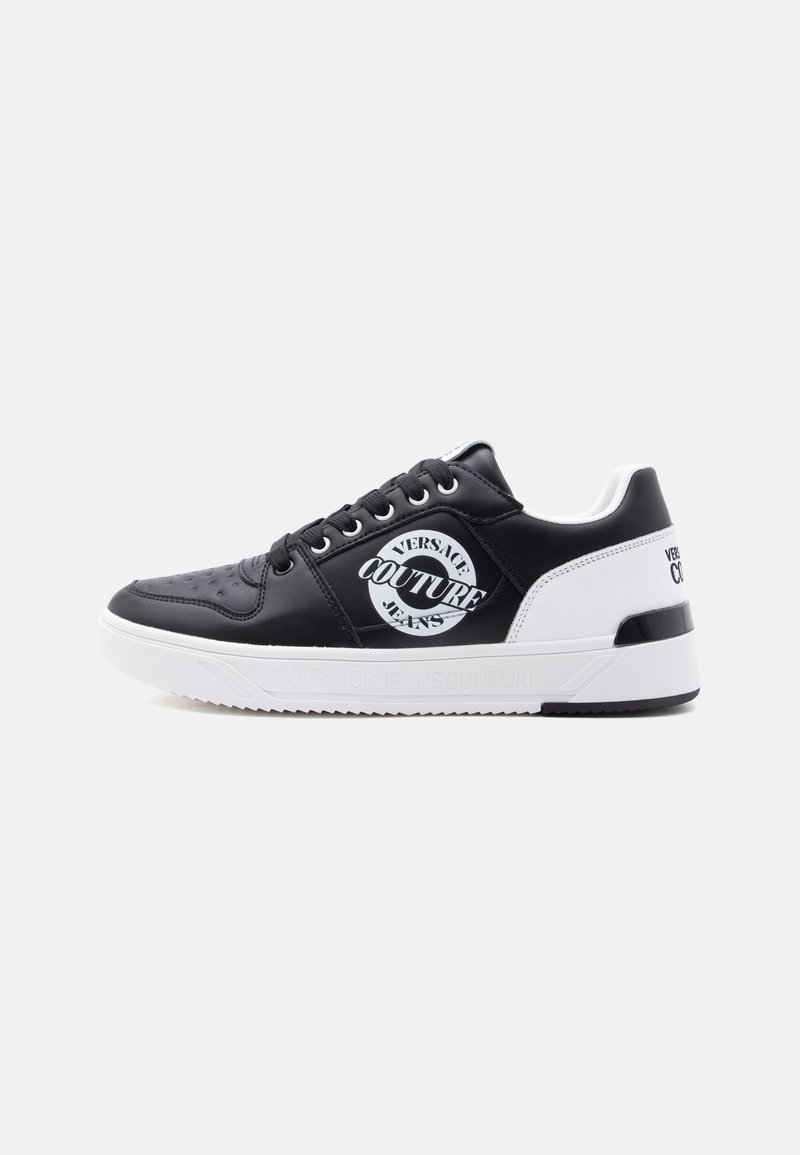 Ανδρικό αθλητικό παπούτσι Versace Couture ασπρόμαυρο με κορδόνια, στρογγυλό λογότυπο στο πλάι και υφή λευκής σόλας σε μονόχρωμο φόντο.