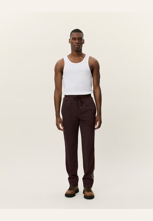 Burgundy jogger pants with a drawstring waist and side stripes. Paired with a white tank top and brown lace-up shoes. Smooth texture.