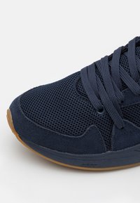 Marinblå sneakers i mesh med tåhätta i mocka, platta skosnören och sula i gumigem. Strukturerad design med öljettdetaljer för andningsförmåga.