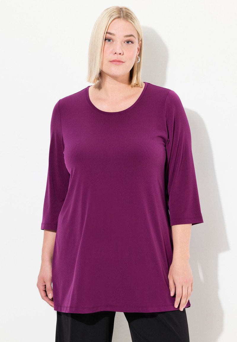 Top viola a maniche tre quarti, realizzato in un tessuto leggero e morbido con scollatura a barca e aderente sulle spalle. Vestibilità casual e rilassata.