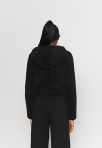 Svart kort hoodie gjord av fluffigt material med huva. Har långa ärmar och en enkel design, med en strukturerad yta.