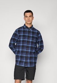 Checked blue and black flannel shirt with long sleeves, button-down collar, two chest pockets, and a straight hem. Features brown buttons.